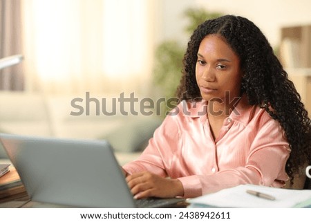 Distracted black tele worker looking away working online at home Royalty-Free Stock Photo #2438942611