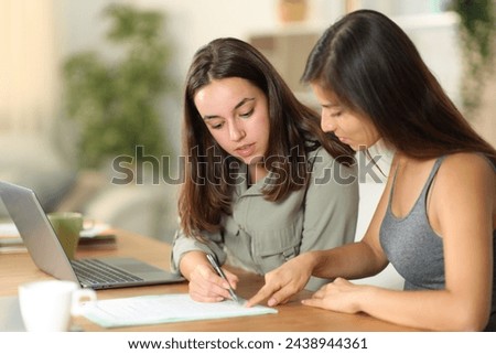 Tele worker explaining where to sign contract to her colleague at home Royalty-Free Stock Photo #2438944361