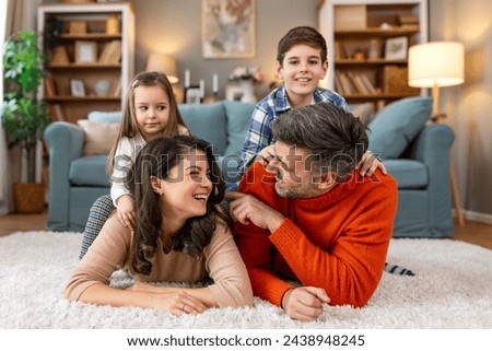 Happy parents and their small kids talking while lying on carpet at home.