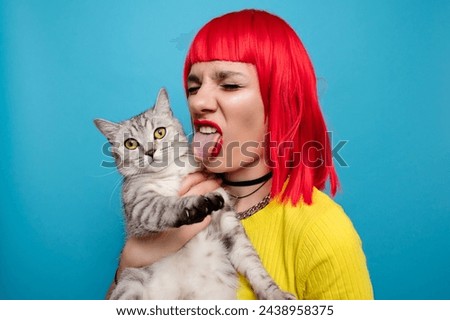 A young beautiful girl with a cat in her arms, isolated on a blue background. Expressive and funny expression on the face. The friendship of the pet and the owner