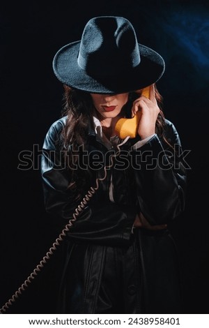 Dark noir portrait of a female detective holding a retro telephone receiver. Private detective, spy, investigation concept.