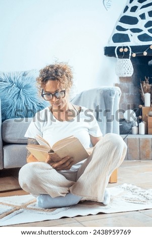 Stay home pastimes. Boomer mature woman sitting on the floor with open book indoors. Beautiful young lady reading exciting story, enjoying lazy morning, having relaxing weekend. Leisure activity
