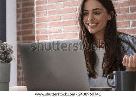 One happy young lady using laptop to videocall friends or business team smiling at the display and gesturing. People and smart working home office workplace lifestyle. Communication with computer Royalty-Free Stock Photo #2438960741