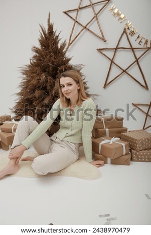 Christmas tree from Pampas grass and handmade presents packed in Kraft paper. Young woman opens Christmas present gift packed in kraft paper. Close up portrait.