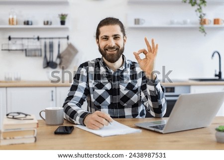 Caucasian consultant offering guidance to clients over digital platform from home, showing sign ok. Smiling business person wearing casual clothes posing with pen, documents and portable computer.