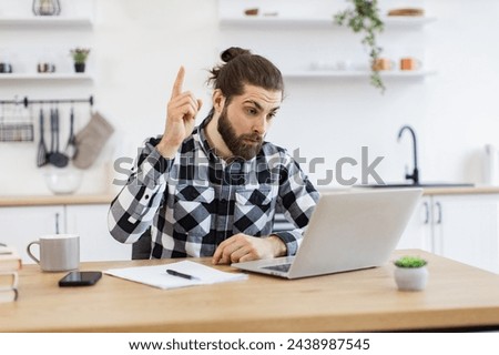 Caucasian professional male running business remotely from home, showing sign of idea, raising finger up. Smiling businessman typing on portable computer while working at wooden desk in dining room.
