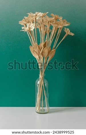 A glass vase with a bouquet of flowers made from straw on the green background.