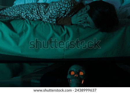 Childhood phobia. Scared girl looking at skull under bed indoors