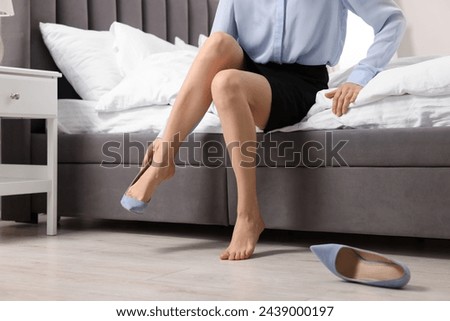 Woman taking off high heels in bedroom, closeup Royalty-Free Stock Photo #2439000197