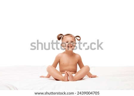 Cheerful little baby, girl in playful pose, sitting up on white mattress with bright smile, fun expression against white studio background. Concept of childhood, motherhood, life, birth. Copy space.