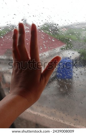 His hand was touching the window glass in the rain, looking like he was upset.