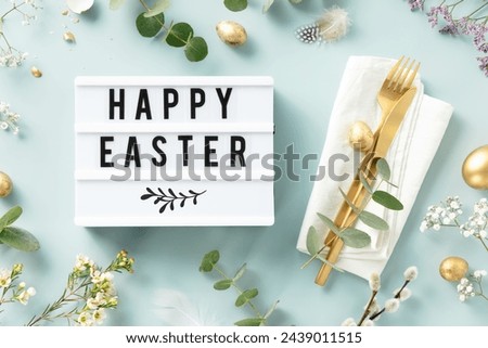 Easter table decorations. Stylish Easter brunch table setting with lightbox text Happy Easter, eggs, vintage cutlery, nests and spring branches on blue background top view flat lay