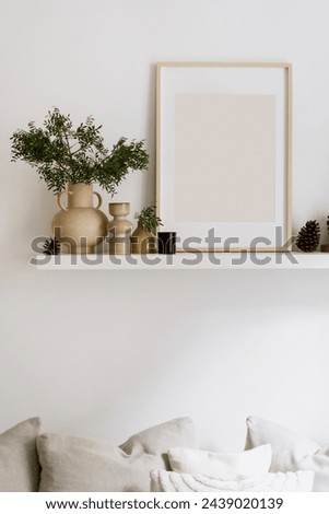 Detail in living room interior, picture in wooden frame with copy space, ceramic vase jug with green plant branch and pine cones on wall shelf. Stylish composition. Home decor idea.