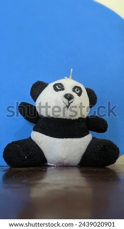 The photo with a blue background of a stuffed panda toy sitting on a shiny wooden table with unclear body proportions makes this toy rare and unique.
