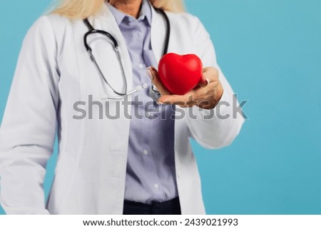 Female doctor in glasses with stethoscope holding heart on the blue background with copy space