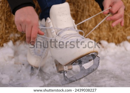 Closeup of a pair of white figure skates being tied and laced up by a pair of Caucasian female hands while resting on the frozen ice rink.