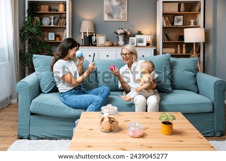 Three generational family together in their living room at home, relaxing with the grandmother. Grandmother and mother in living room with baby smiling. Multi-generation family portrait Royalty-Free Stock Photo #2439045277