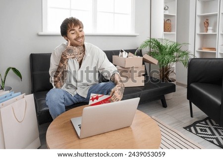 Thoughtful young man with gift voucher and laptop shopping online at home