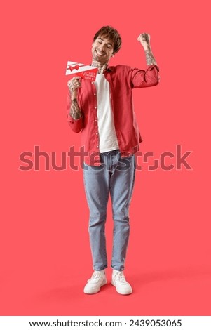 Happy young tattooed man with gift voucher on red background