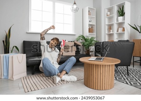 Happy young tattooed man with gift voucher sitting at home