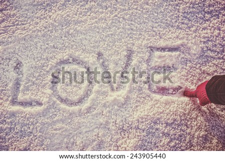 written or drawn by hand in pink glove word LOVE on white snow, romantic image composition, vintage photo. Human hand write or drawing letters on snow in winter time