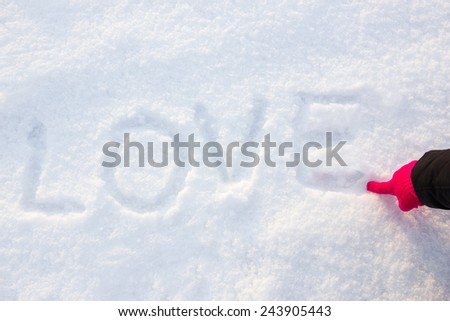 written or drawn by hand in pink glove word LOVE on white snow, romantic image composition. Human hand write or drawing letters on snow in winter time