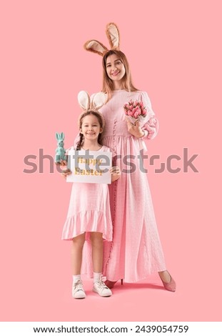 Cute little girl with card her mother in bunny ears on pink background. Easter celebration