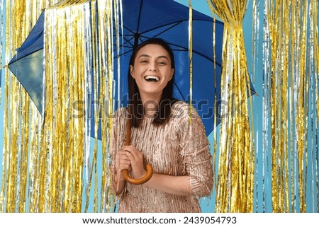 Young woman with umbrella and tinsel on blue background