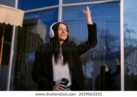 A woman in a suit and headphones dances cheerfully on the street, singing along to music, embodying joy and positivity. A freelancer enjoys the freedom of flexible work hours.
