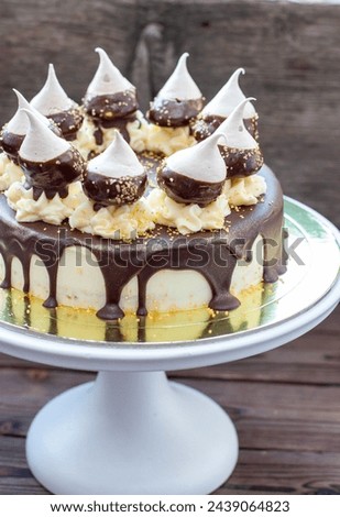 Birthday cheesecake decorated with melted dark chocolate sauce, meringues and butter cream swirls on white cakestand. Rustic background Royalty-Free Stock Photo #2439064823