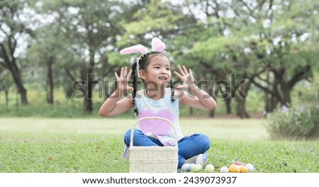 Happy cute little Asian child girl hunting Easter eggs, wearing bunny ears. kid counting eggs in basket after play hunt eggs game while playing outdoors at park