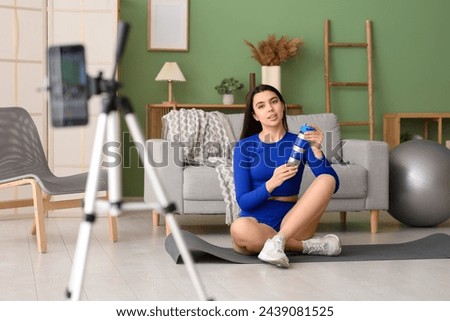 Female blogger with water bottle recording sports video at home