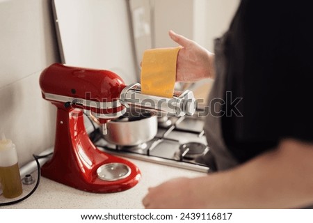 A person using a vibrant red electric pasta maker to prepare homemade noodles. Royalty-Free Stock Photo #2439116817