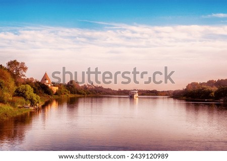 Beautiful morning landscape of the banks of the Volkhov River. In the distance is a cruise ship and a medieval fortress Royalty-Free Stock Photo #2439120989
