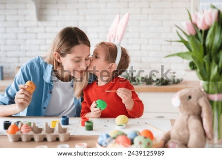 Little cute son kissing his mom while painting eggs for Easter in the kitchen. Easter springtime holiday celebration. Young family of two decorating ornaments for fest at home