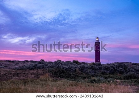This captivating image showcases a lighthouse bathed in the fading light of twilight, standing tall amidst the wild heath. The dusky sky transitions from deep blue to soft pink and purple hues, adding Royalty-Free Stock Photo #2439131643