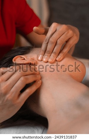 Close-up of the hands of a masseur doing facial massage to a young brunette woman in a spa salon. Concept of health and beauty. Vertical photo
