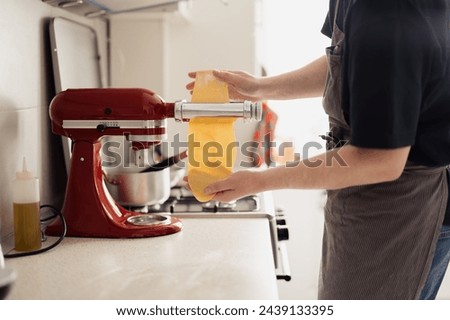 Close-up of hands using a stand mixer to prepare fresh pasta dough in a home kitchen. Royalty-Free Stock Photo #2439133395