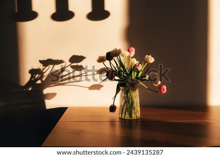 Bouquet of white and pink tulips in a transparent vase on wooden table. Spring background with a bouquet of flowers. Front view
