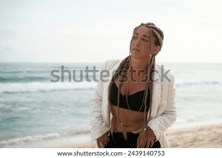 Portrait of a young Latino woman with braids on her head. She walks along the beach near the ocean in a jacket and suit. Self confidence and masculinity concept. Braiding studio. Royalty-Free Stock Photo #2439140753