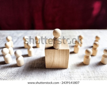 Wooden toy doll on high pedestal and many other figures below. Concept of leadership, which is not available to everyone. Victory and the winner. Talent, Recruitment employee and Successful business Royalty-Free Stock Photo #2439141807