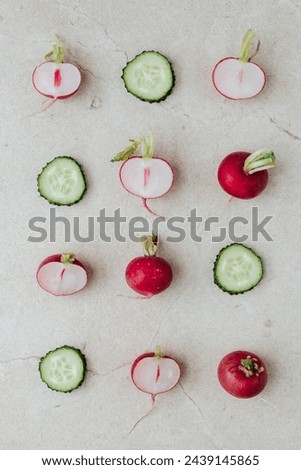 halves of radishes and whole radishes and cucumber slices are laid out in even rows on a beige stone background