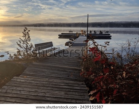 A dock reaches out onto a calm misty lake in the fall during sunrise