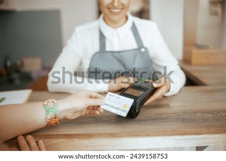 Closeup on woman hair salon employee in modern hair studio with client accepting credit card payments via terminal on reception.