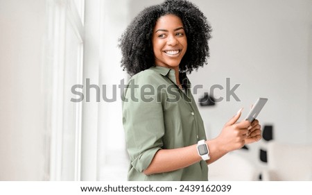 Beaming with happiness, an African-American woman holds and operates a tablet, her engagement with the device suggesting a pleasant online experience in a comfortable and bright interior setting Royalty-Free Stock Photo #2439162039