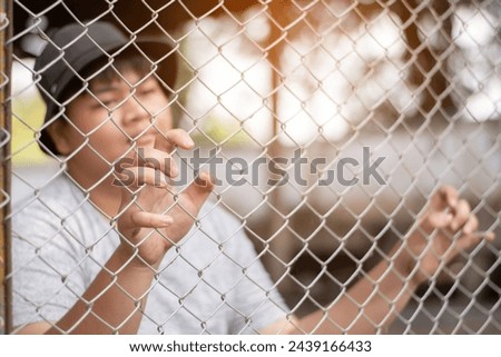 Asian teenboy sitting and holding big metal fence panel in front of a juvenile detention facility, awaiting further release with friends sadly, freedom and detention of people concept. Royalty-Free Stock Photo #2439166433