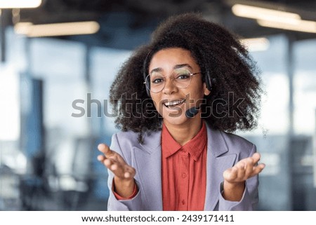 Portrait of successful lady with bushy hairstyle wearing wireless headset with microphone and looking at camera. Optimistic coach remotely presenting motivating speech for freshly recruited trainees.