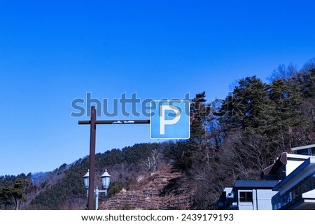 Parking (P) sign mounted on brown steel beam. Mountains, blue sky and bright sunlight in the background. Symbol aluminum white, blue post about Parking sign car showing free places. traffic sign