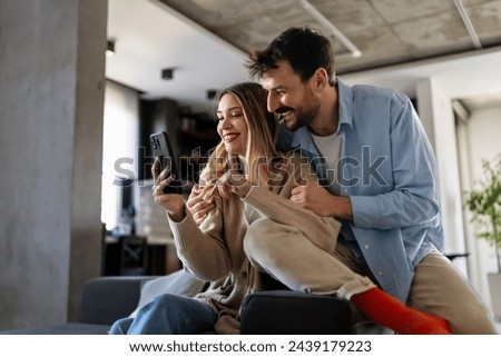 Smiling couple embracing while looking at smartphone. People sharing social media on cellphone.