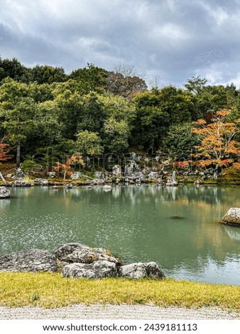 Autumn landscape in Kyoto. Mesmerising view at the lake with colourful trees on the background. Leaves are coloured in red, orange, yellow astonishing colours. Dramatic sky are above this calm, serene